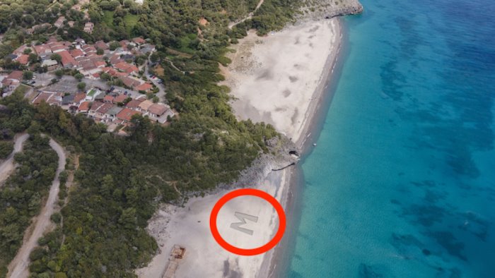 camerota compare una m gigante sulla spiaggia